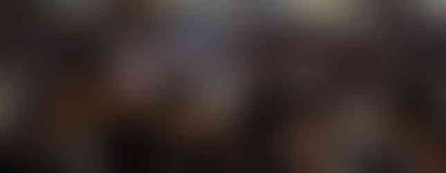 Audience attentively listening in a dimly lit church, with some faces illuminated. A "Book Store" sign is visible in the background.