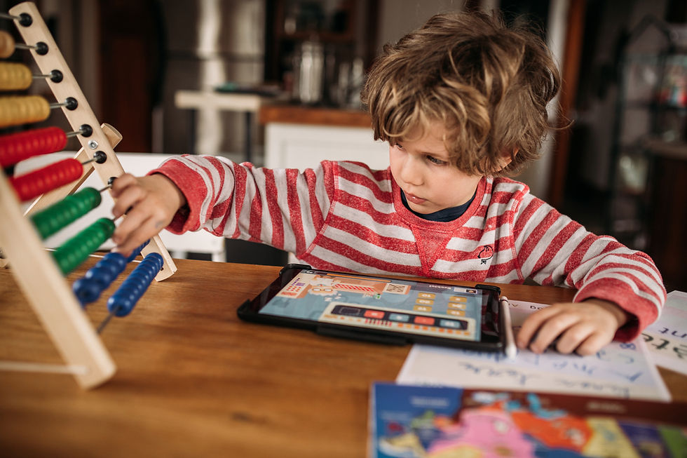 Child in a red-striped shirt using an abacus and tablet at a wooden table, focused and engaged. Books and papers are nearby.
