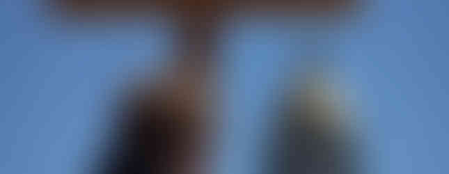 A man carries a large wooden cross while facing the Colorado State Capitol building under a clear blue sky.