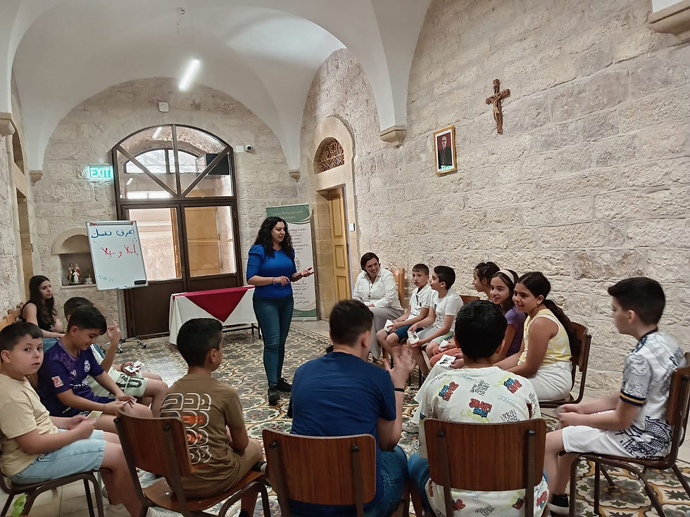 A woman engages kids seated in a circle in a stone-walled room. An easel displays text. The mood is interactive and focused.