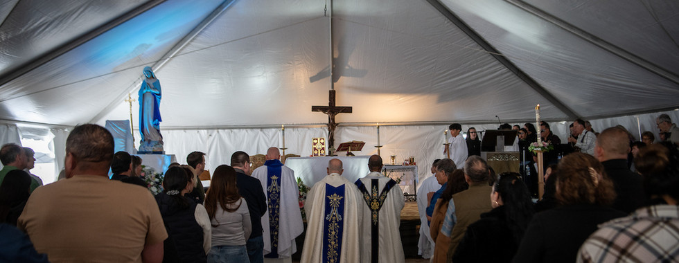 Priests process toward an altar during Mass celebrated inside a large white tent filled with parishioners.