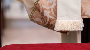 Elegant ivory and gold-patterned fabric with fringe detail hangs over a red textured surface, creating a refined, serene atmosphere.