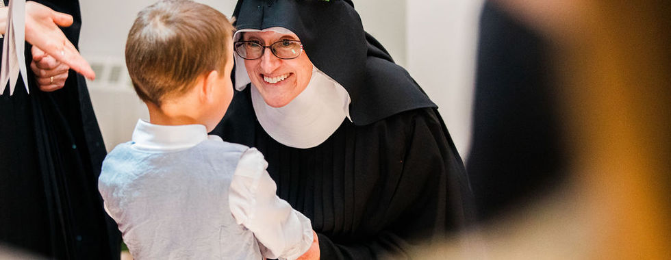 A joyful newly professed sister smiles and speaks with a young child during the reception after Mass.