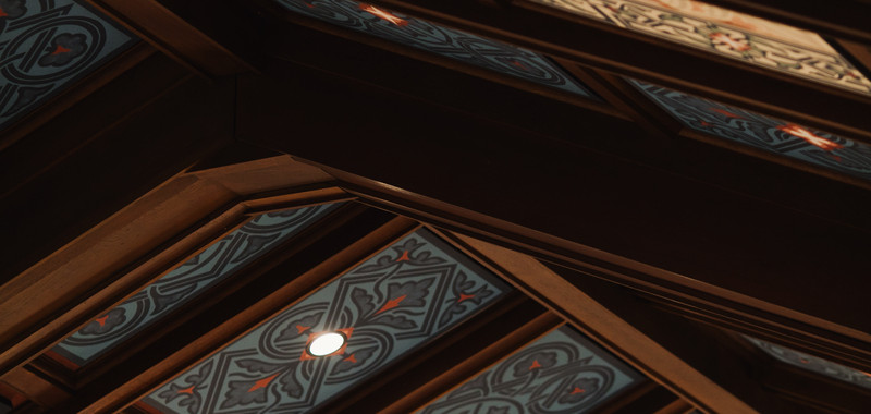 Ornate patterned ceiling panels with warm wood beams and small recessed lights in a dark, elegant interior.
