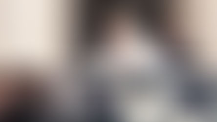 A man in white robes, standing in a vehicle, touches his chest, surrounded by people. A cameraman films nearby. Bright, outdoor setting.