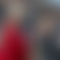 A man in a red robe and white mitre is blessing a woman holding palm fronds on a city street, surrounded by onlookers.