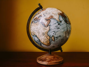 A globe on a wooden table against a yellow wall, showing Africa and the Indian Ocean. The image has a warm, nostalgic feel.