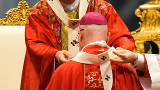 Two Catholic clerics in ornate red vestments during a solemn ceremony, one placing a stole on the other before a gold altar.