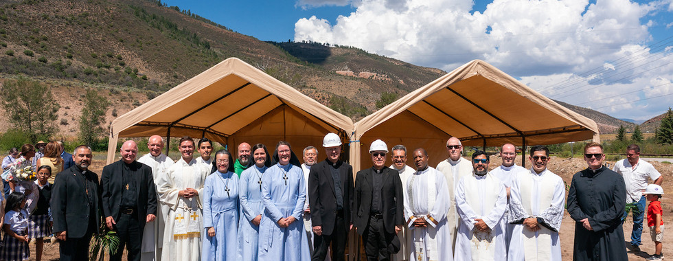 Group of clergy and religious leaders posing outdoors under beige tents in a mountain valley on a bright sunny day