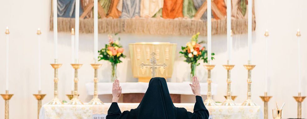 A newly professed religious sister raises her hands in prayer before the altar during the celebration.