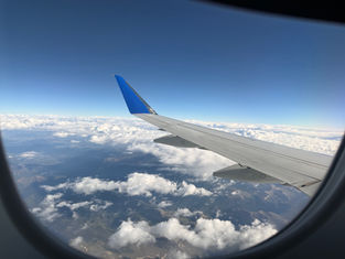 Airplane wing seen from a window above white clouds and mountains under a clear blue sky, calm and expansive view