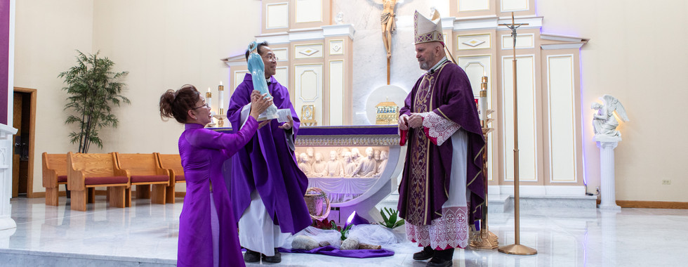 Clergy in purple vestments hold a statue in a church with a crucifix backdrop. A woman in purple gown participates, creating a reverent mood.