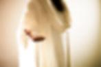 Outstretched hand in white robe, highlighting a small metallic object, warm glowing background, serene and inviting atmosphere.