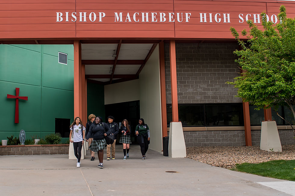 Estudiantes con uniformes salen del edificio Bishop Machebeuf High School. Fondo con cruz roja y paredes verdes. Ambiente relajado.