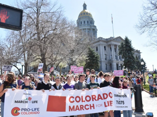 Crowd holds "Colorado March for Life" banner outside the Colorado State Capitol. Participants carry signs, showing a peaceful protest.