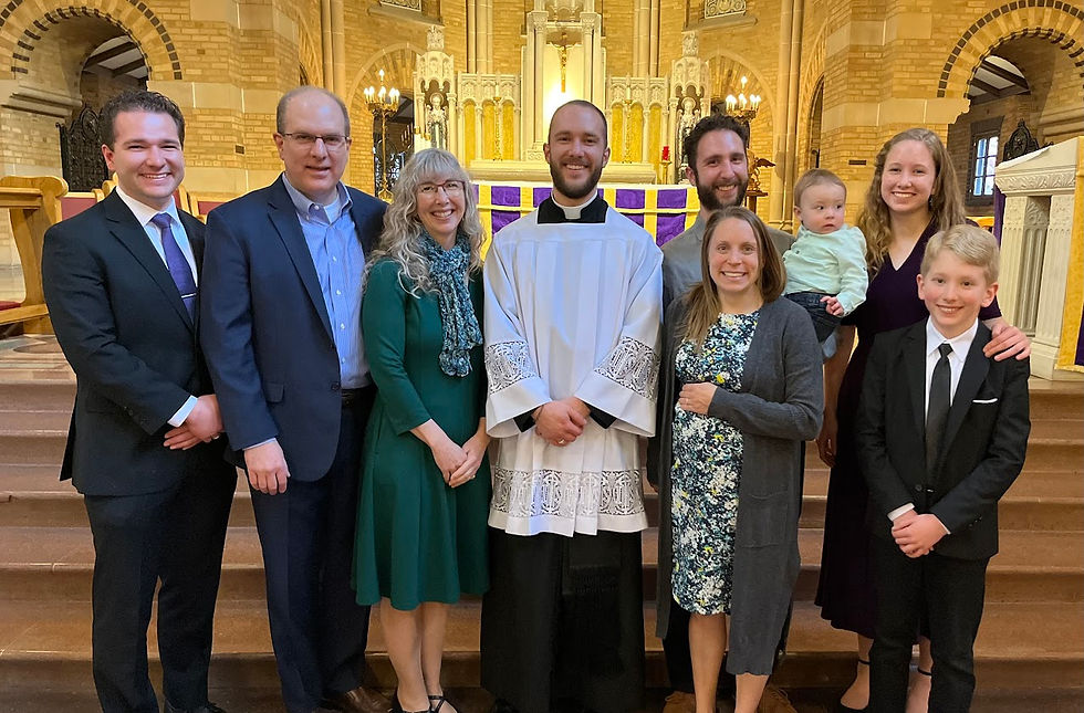 Grupo de personas sonrientes en iglesia, incluyendo un hombre con vestimenta litúrgica blanca, fondo de altar dorado y velas encendidas.