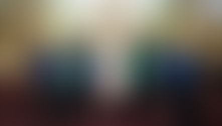 A group of people in a church setting wearing black attire with blue and green sashes, standing in front of an ornate altar and wood paneling.