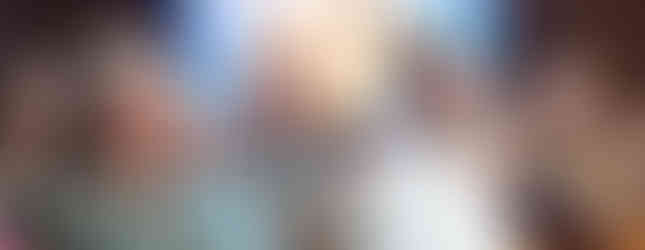 Audience seated in a church, listening attentively. A person in a white robe sits beside those in casual attire. Stained glass in background.