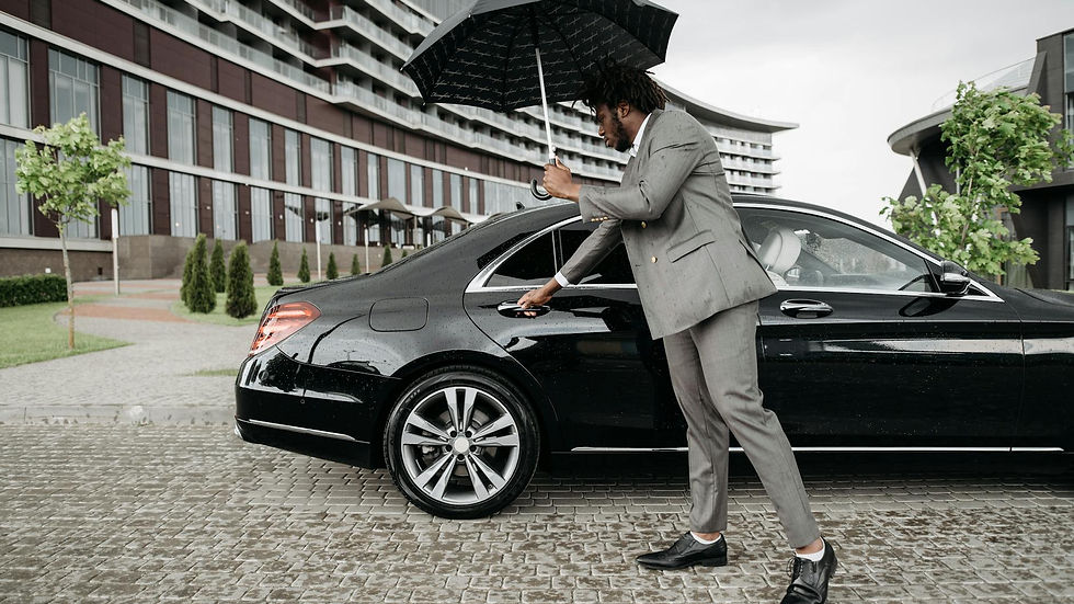 Elegant man in suit opens car door under umbrella by modern building on rainy day.