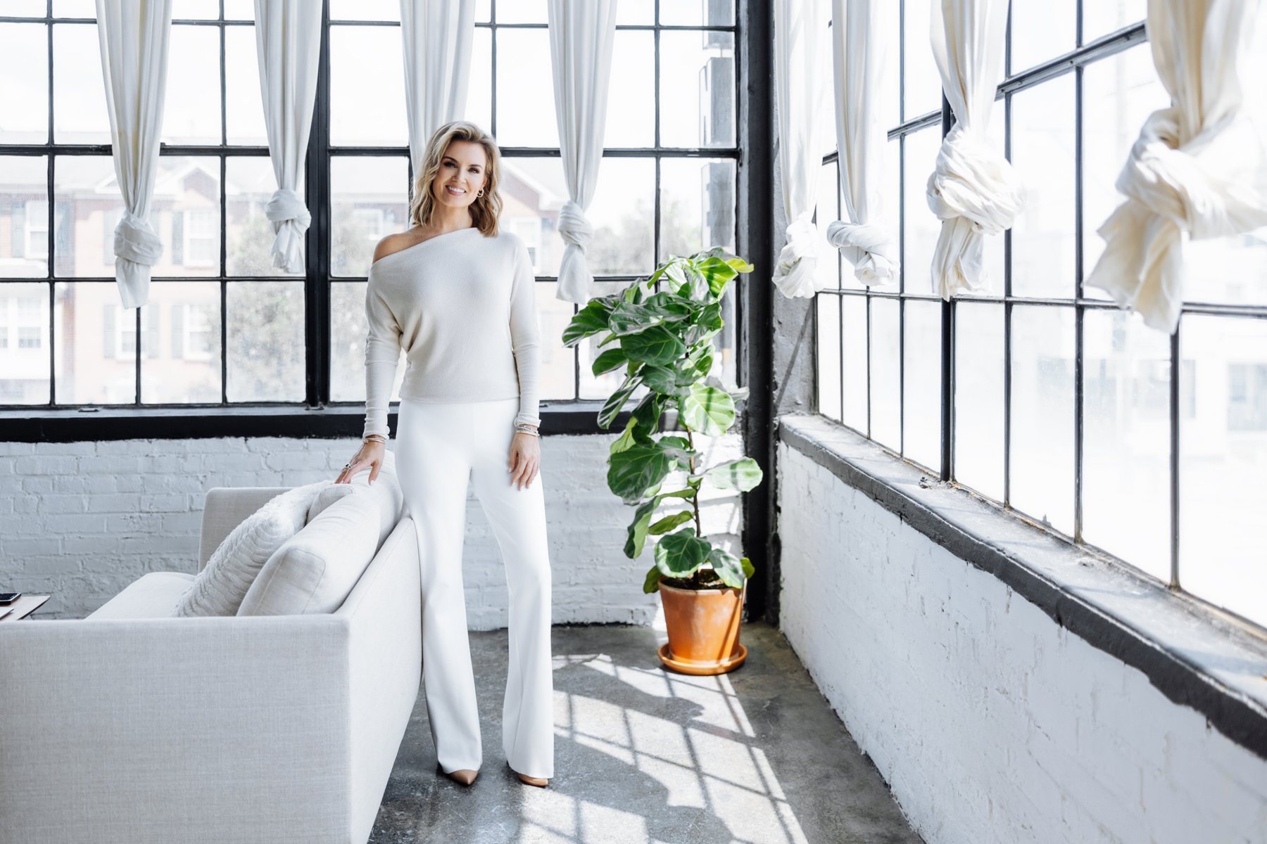 Jillian standing beside a white couch by tall windows, smiling