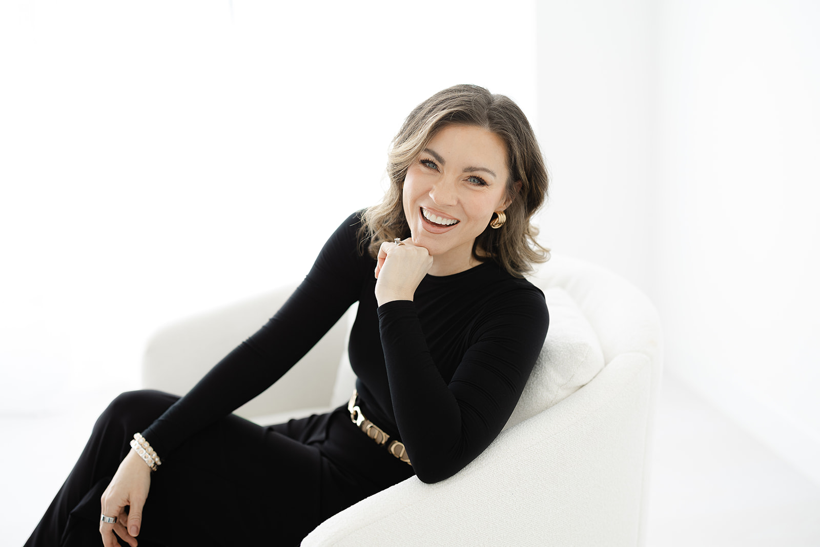 Erin Stringer laughing in a white armchair, in a black top