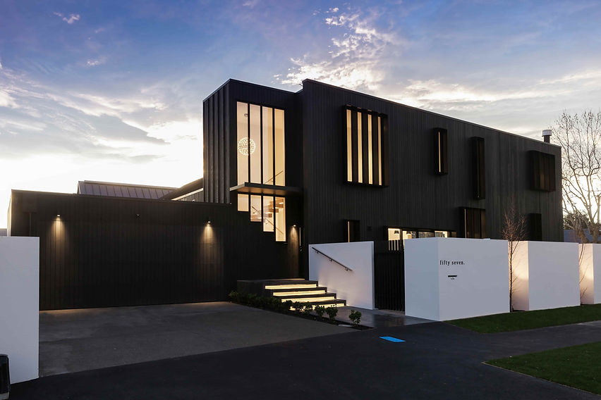 Exterior photo of large architectural home at dusk with warm fence and garage feature lighting and view to large exposed internal staircase and round feature pendant light