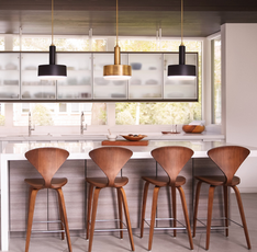 Modern kitchen with three Cedric by Hinkley pendant lights—two in matte black and one in aged brass—hanging above a white island with wooden bar stools.