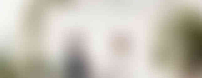 Bride and groom stands under a modern minimalist chuppah with white florals. drapes, and greenery