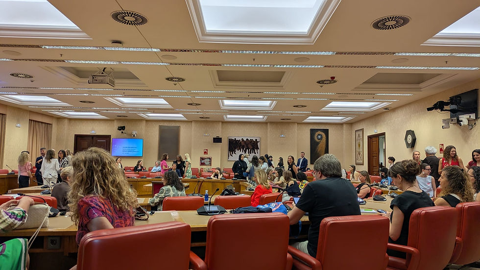 Sala de reuniones con muchas personas conversando; sillas rojas, pantallas y tragaluces, ambiente animado.
