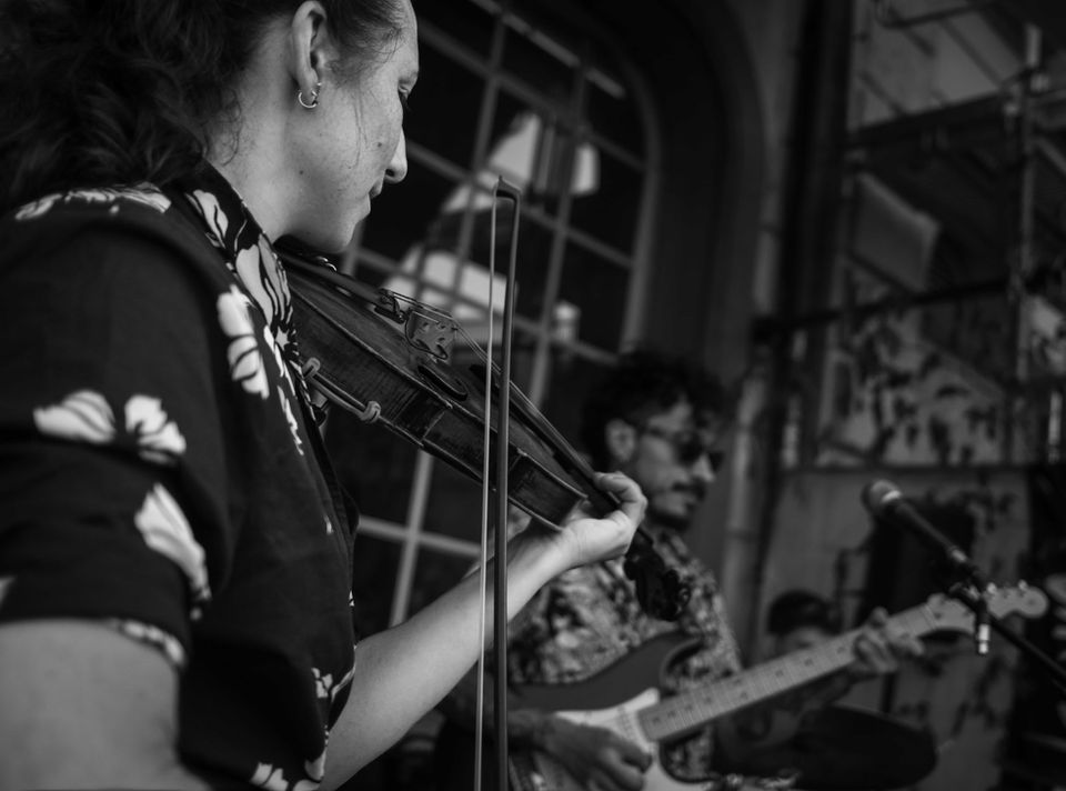 A woman plays the violin in the foreground, a man plays the guitar in the blurred background, black and white photograph.