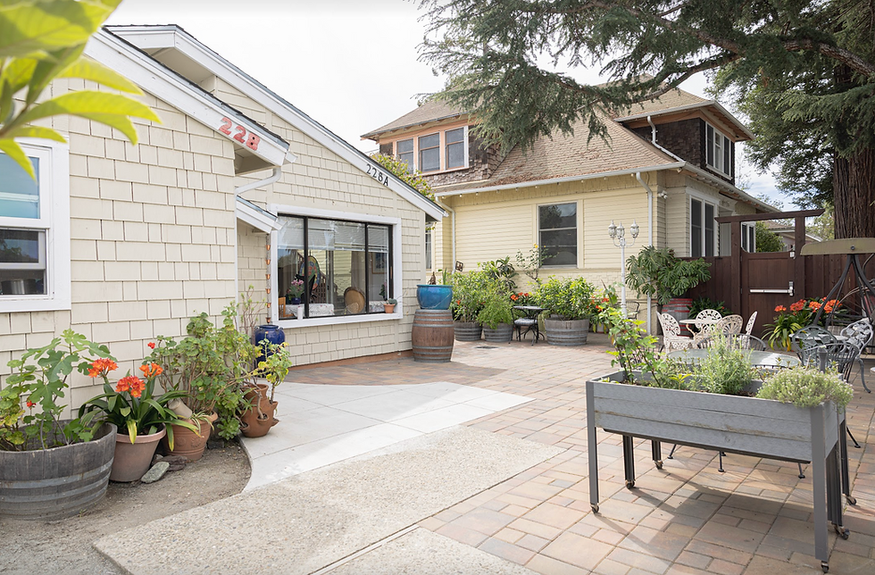 Our community is made up of two neighboring houses — joined together by this sunlit courtyard. Both homes are part of Alexandria Victoria, and residents, families, and staff move freely between them. The courtyard, with its raised garden beds, café tables, and potted flowers, is the heart that ties the two houses into a single, connected home.