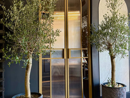 Loft-Tür mit Bogenform im italienischen Restaurant in Berlin, gefertigt aus Stahlprofil RAL1036 PerlGold mit kombiniertem Glas – transparent außen, strukturiert innen, als zentrales Designelement des Raums.