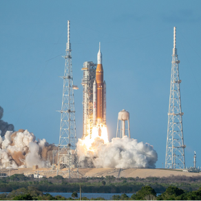 A rocket launches amidst smoke and flames, surrounded by tall towers under a clear blue sky, conveying excitement and power.