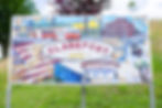 Mosaic sign with "Glassport 1902" text, depicting a red brick building, trolley, and flag design. Set in a grassy area with trees in the background.