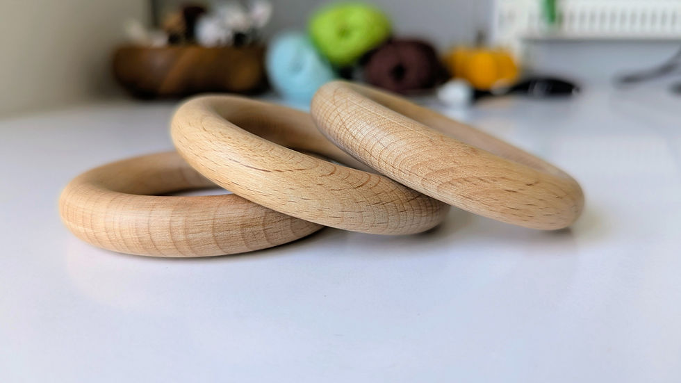 Three beech wooden rings intertwined on a white surface, with colorful yarn balls blurred in the background