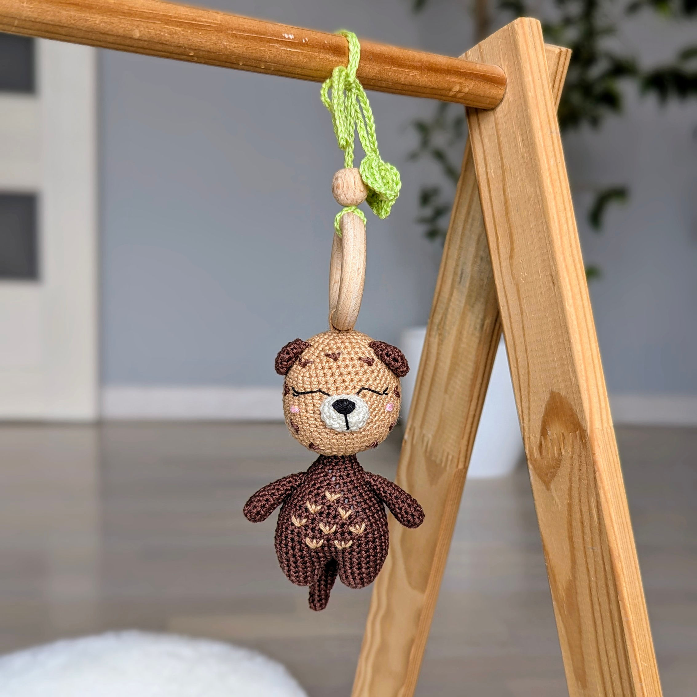 Handmade crochet hanging toy with soft otter attached to baby gym using green string loop — warm caramel and chocolate tones