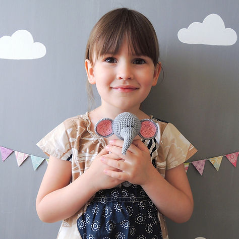 A little girl is holding a soft toy elephant in her hands.