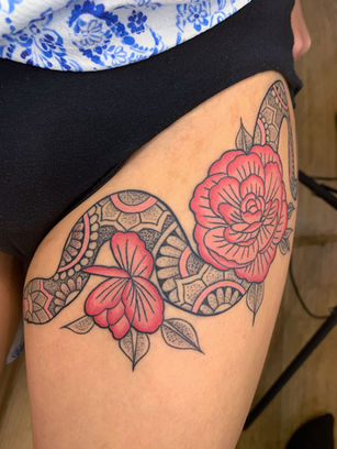 Ornamental snake tattoo wrapped around pink peony flowers with geometric pattern detailing on the thigh.