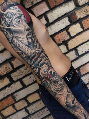 Black and grey Japanese samurai sleeve tattoo with koi fish, waves, and red accent highlights on the arm.