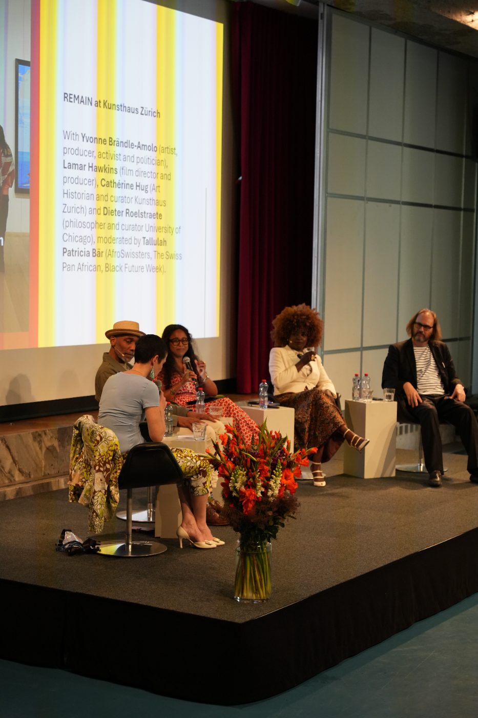 Cathérine Hug speaking on stage, with Lamar Hawkins, Tallulah Patricia Bär, Yvonne Apiyo Brändle-Amolo and Dieter Roelstraete