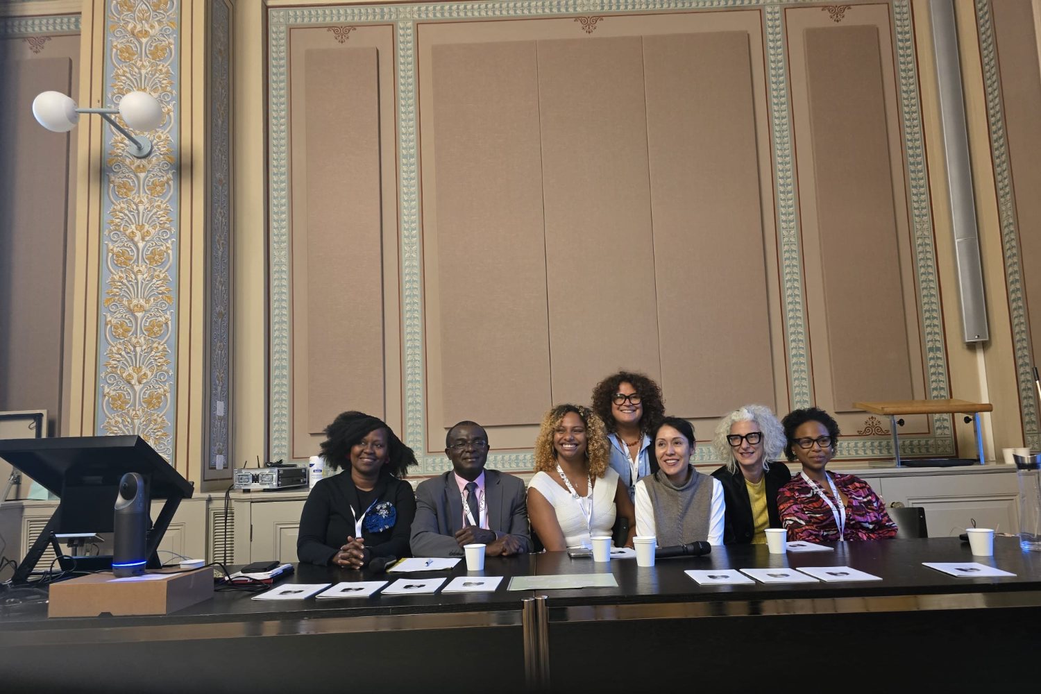 Seven people at the roundtable, some seated and some standing behind the table
