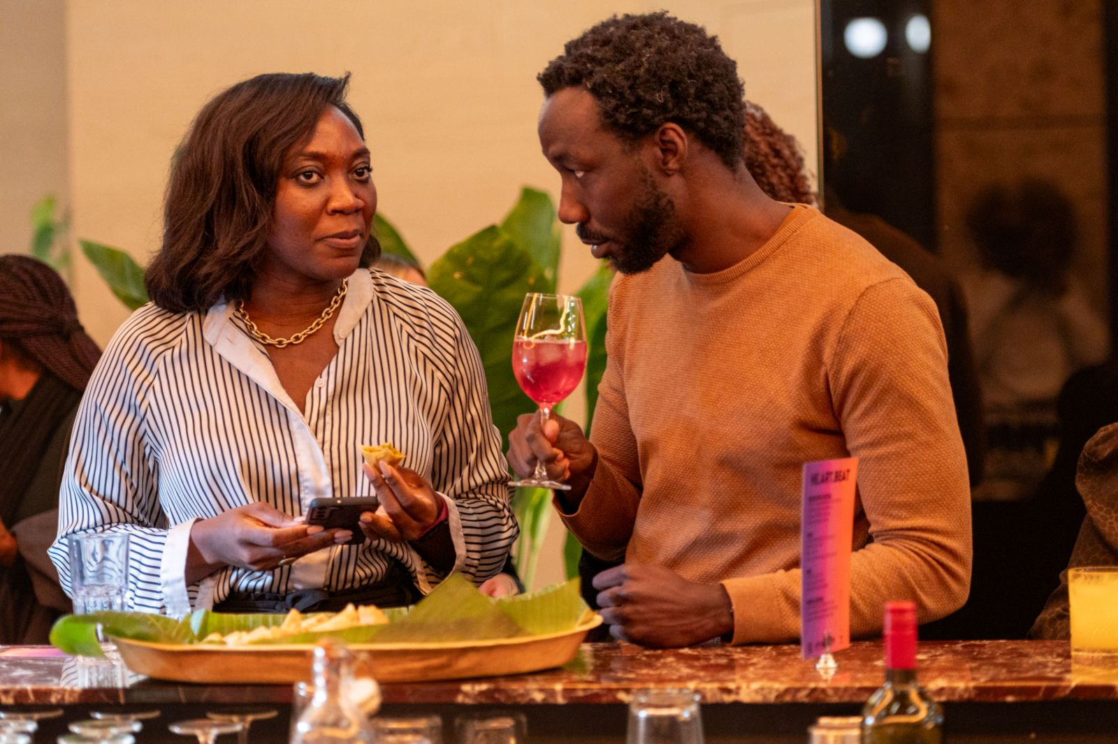 Two guests talking at the bar, one holding a pink drink