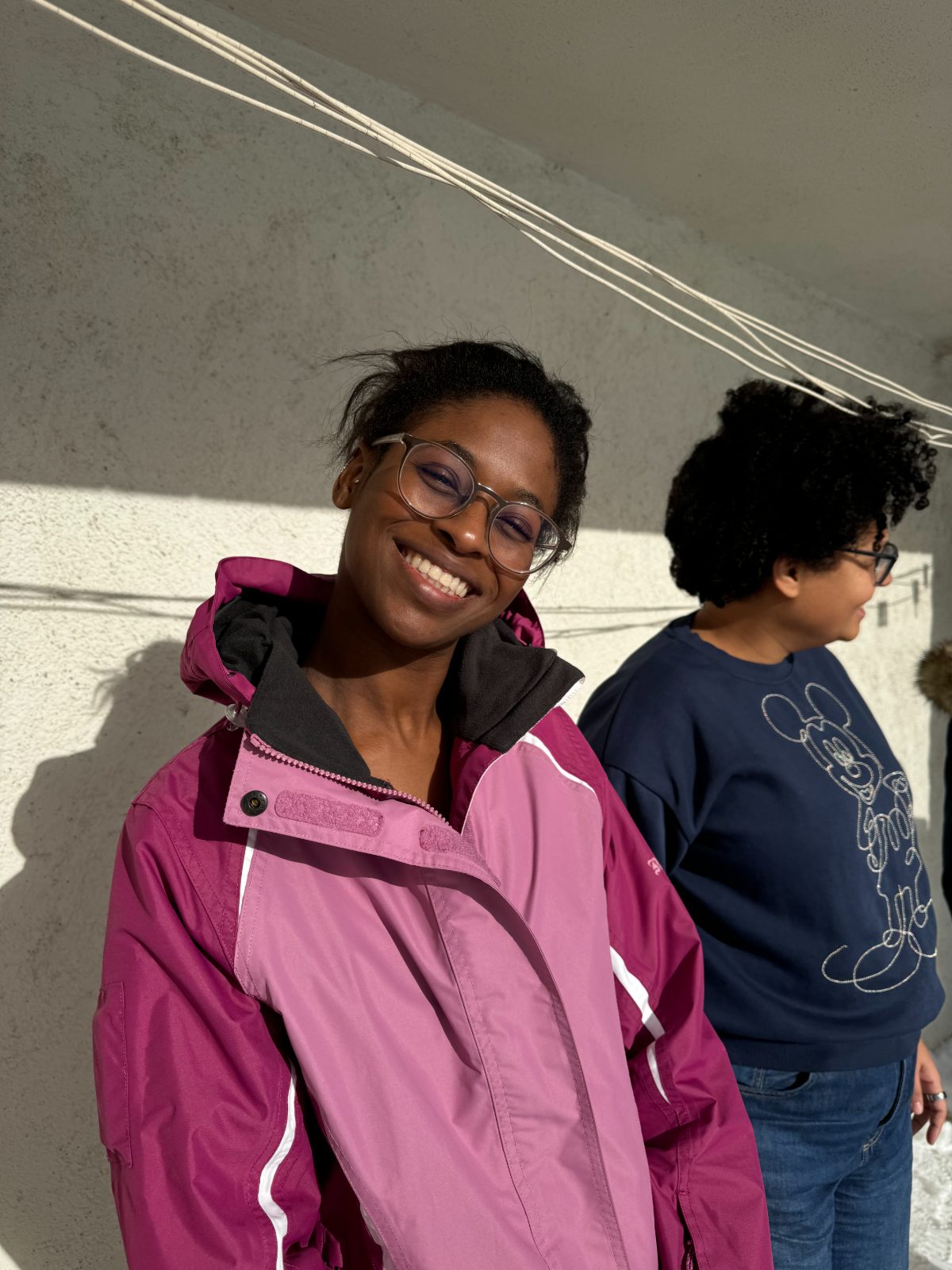 A woman in a pink jacket smiling, another woman beside her looking away