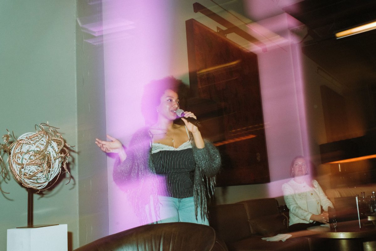 Artist and curator Christin Khaukha with a microphone beside a wire sculpture, in pink light