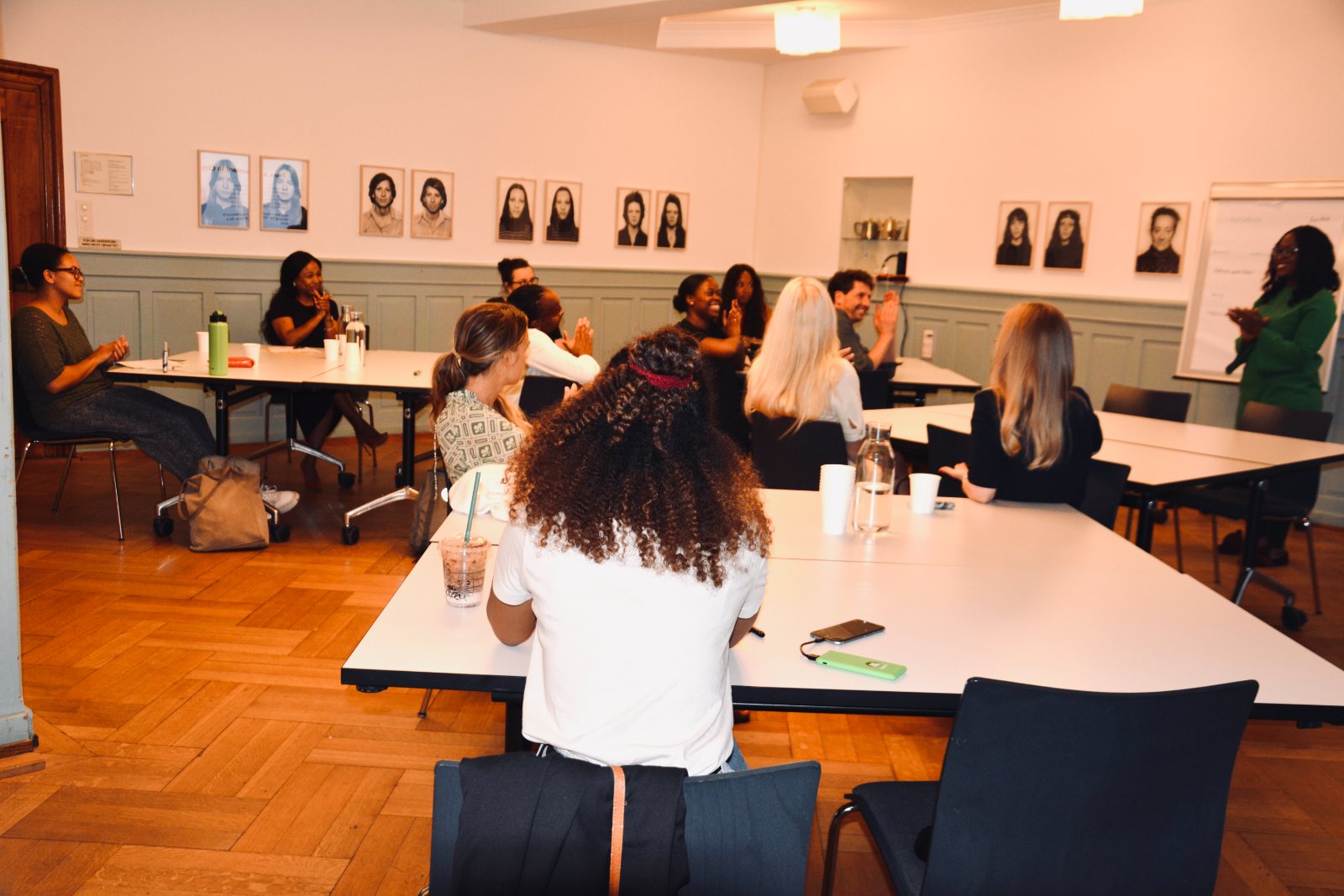 Participants at long tables in a room hung with portrait drawings