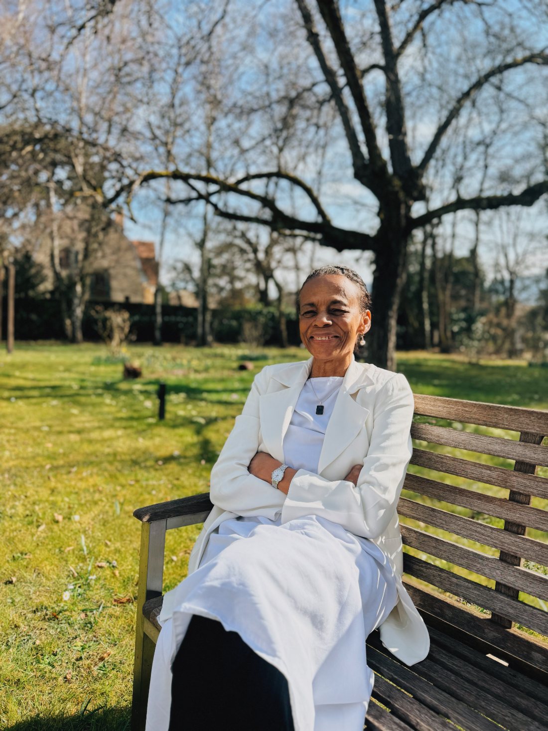 Carmel Froehlicher in a white suit, sitting on a bench in a sunny garden