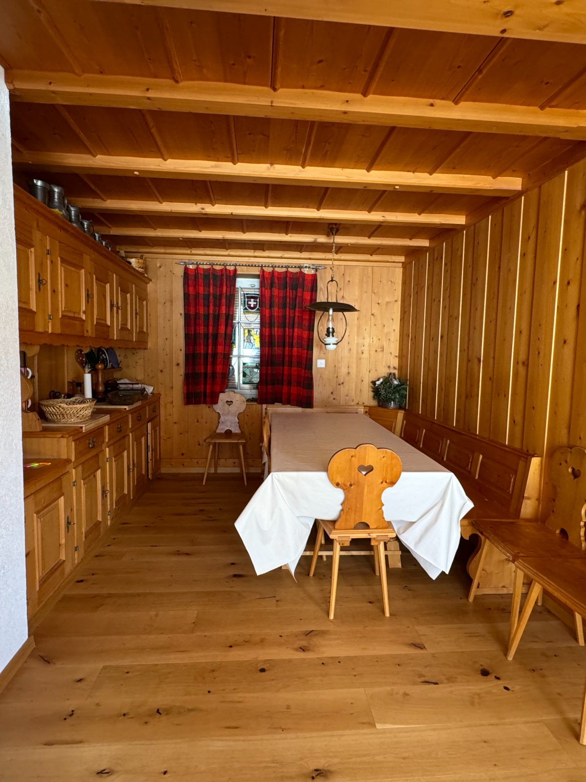 A wood-panelled dining room with a long table and red checked curtains