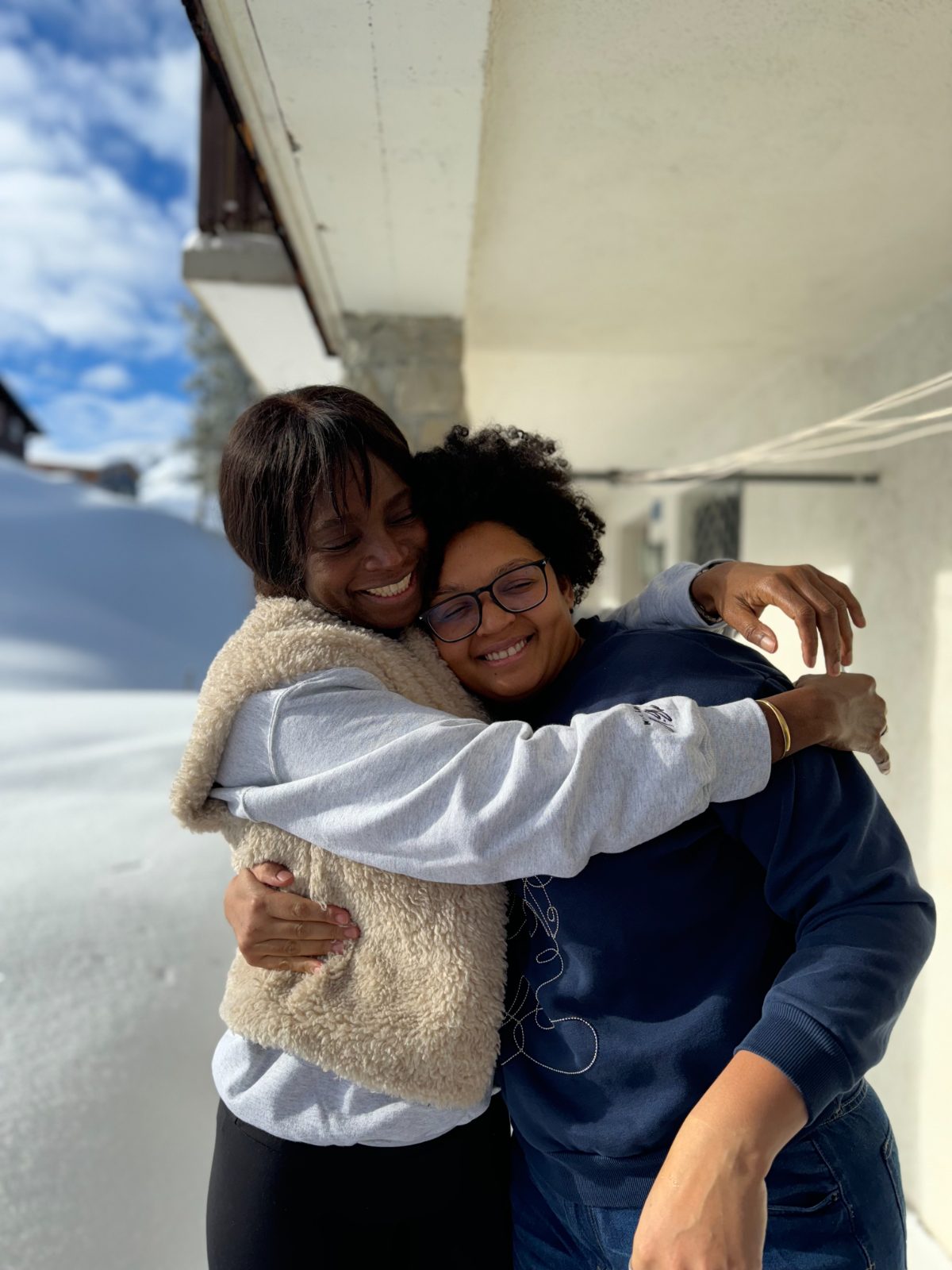Two women hugging and smiling outside a house in the snow