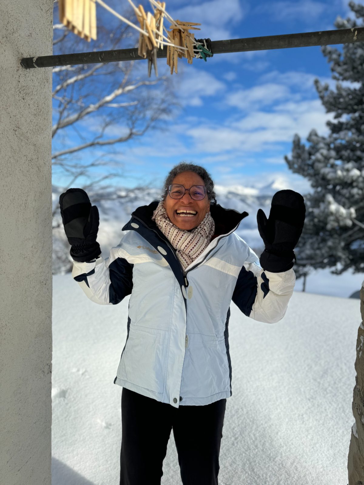 A woman in a white ski jacket and mittens laughing with her hands raised in the snow
