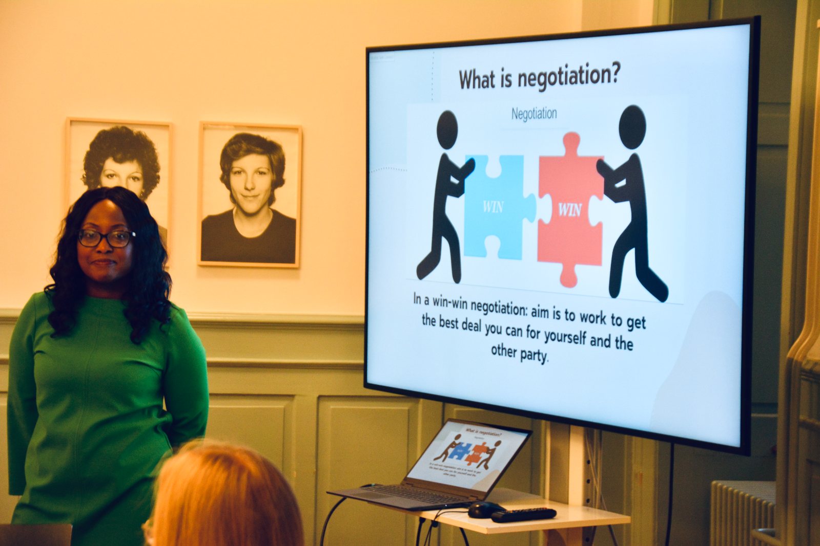 Claudia Bruce Quartey in a green dress beside a screen that reads What is negotiation?